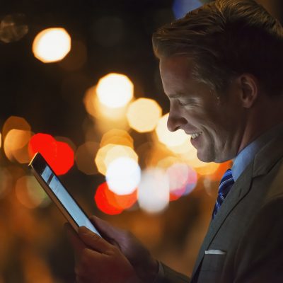 A man in a city at night, looking at a computer tablet.